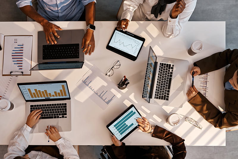 Group of people meeting at a large table on their digital devices