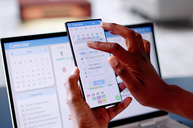 Person viewing digital calendar on laptop screen as well as phone